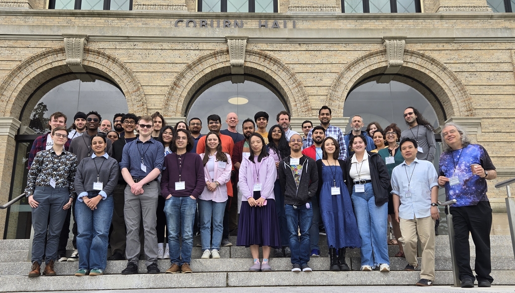 A group of about 40 people       standing on steps in 4 rows outside a building with the words       Corbon Hall